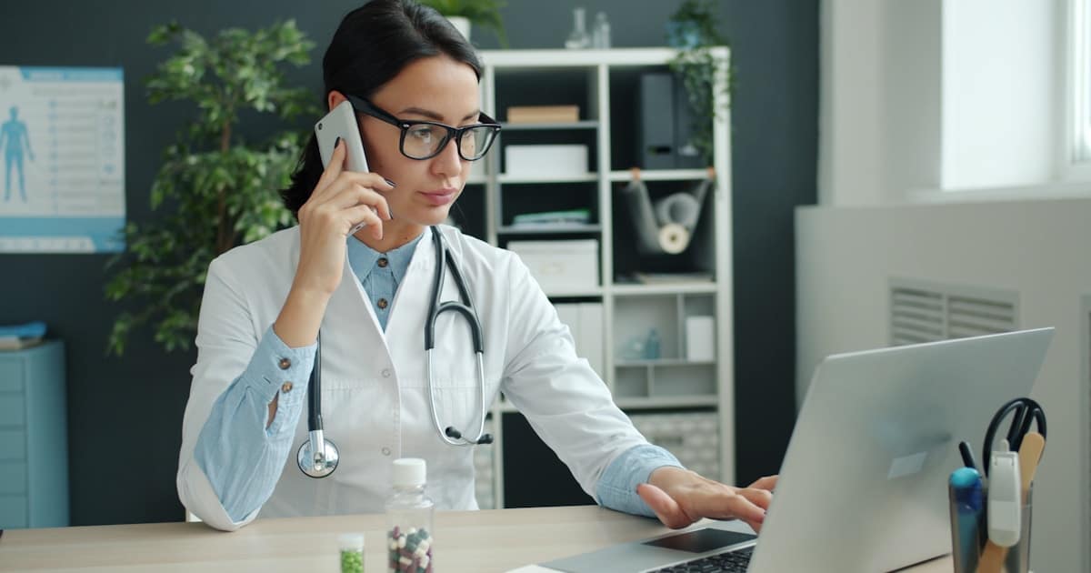 Médica especialista em consultório particular consultando laptop para gerenciar o site profissional